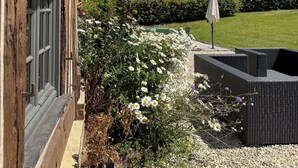 Ein Holzkonstrukt mit einem Fenster, ein Garten mit weißen Blumen und ein klarer, blauer Himmel.
