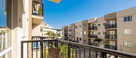 Ein Balkon mit einem Korbstuhl, einem Blumentopf und Blick auf ein Wohngebiet mit mehreren Wohnhäusern.