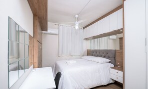 Un dormitorio con cama, escritorio, espejo y ventilador de techo.