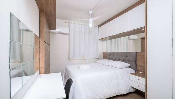 A bedroom with a bed, a desk, a mirror, and a ceiling fan. - Apt in Cond. c/ Pool 5min From the Beach Mar202 (Florianópolis)
