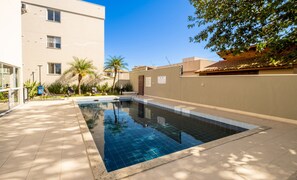 A swimming pool with tiled edges, surrounded by a beige building and palm trees. - Apt in Cond. c/ Pool 5min From the Beach Mar202 (Florianópolis)