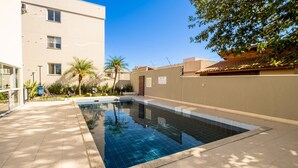 A swimming pool with tiled edges, surrounded by a beige building and palm trees. - Apt in Cond. c/ Pool 5min From the Beach Mar202 (Florianópolis)