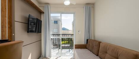 Una sala de estar moderna con un sofá, un televisor montado en la pared y un ventanal corredero que da a un espacio exterior.