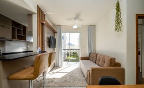 A modern kitchen with a bar area, a sofa, and a dining table. - Apt in Cond. c/ Pool 5min From the Beach Mar202 (Florianópolis)