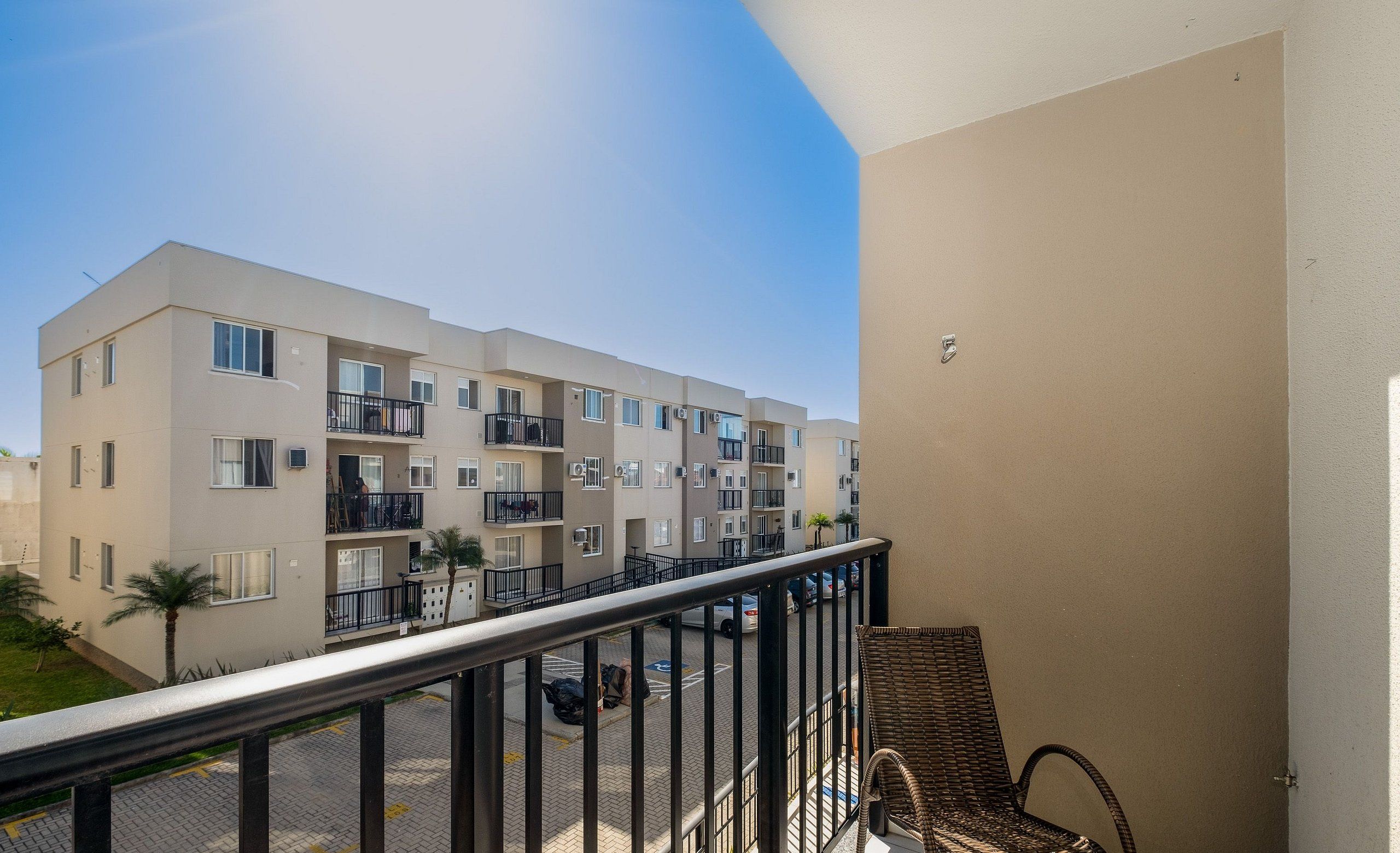 A multi-story residential building with balconies, a paved ground floor, and a clear sky.