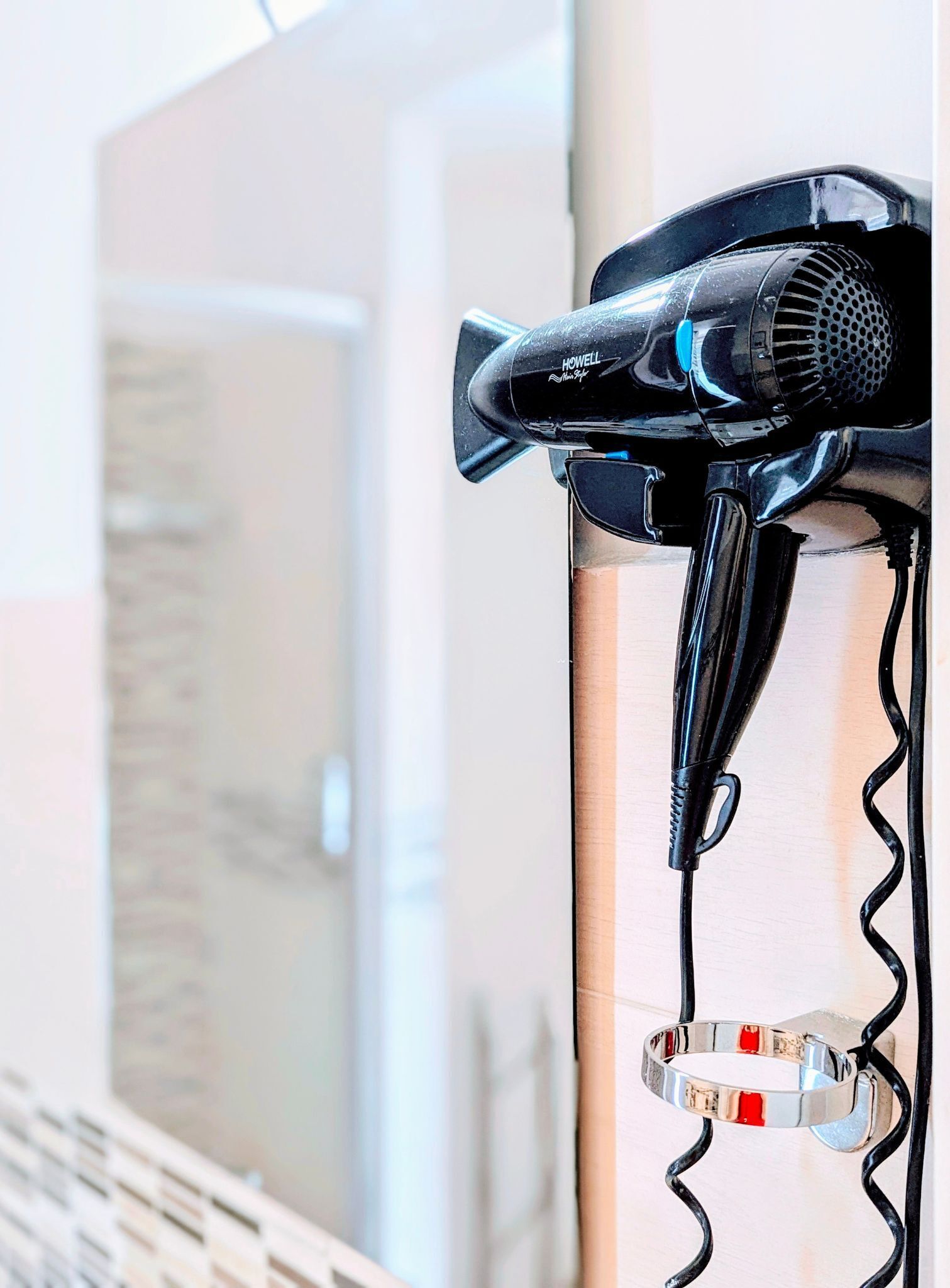 Un sèche-cheveux fixé au mur de la salle de bain, avec une serviette suspendue en dessous.