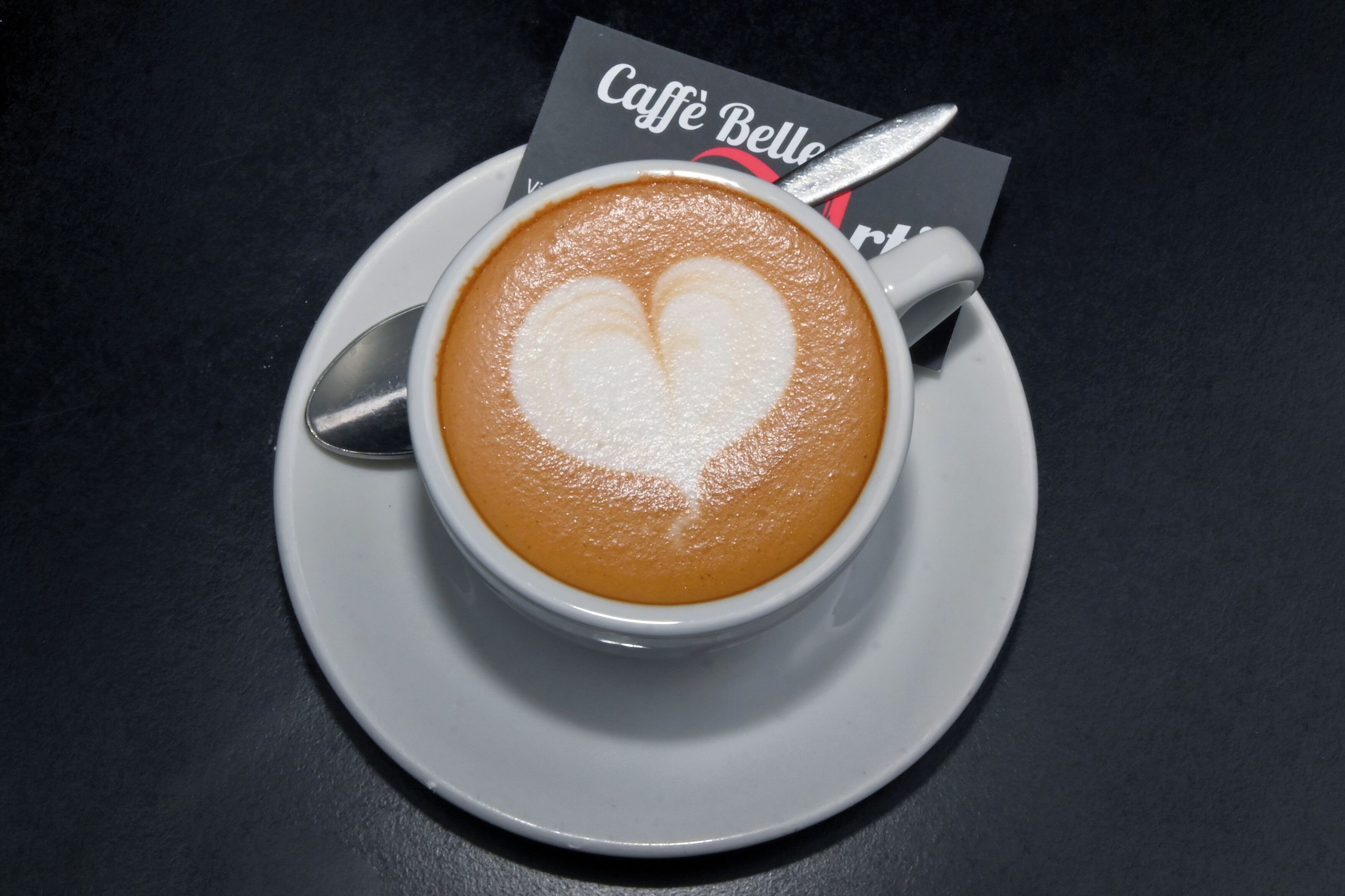 A cup of coffee with a heart-shaped latte art on a white saucer.