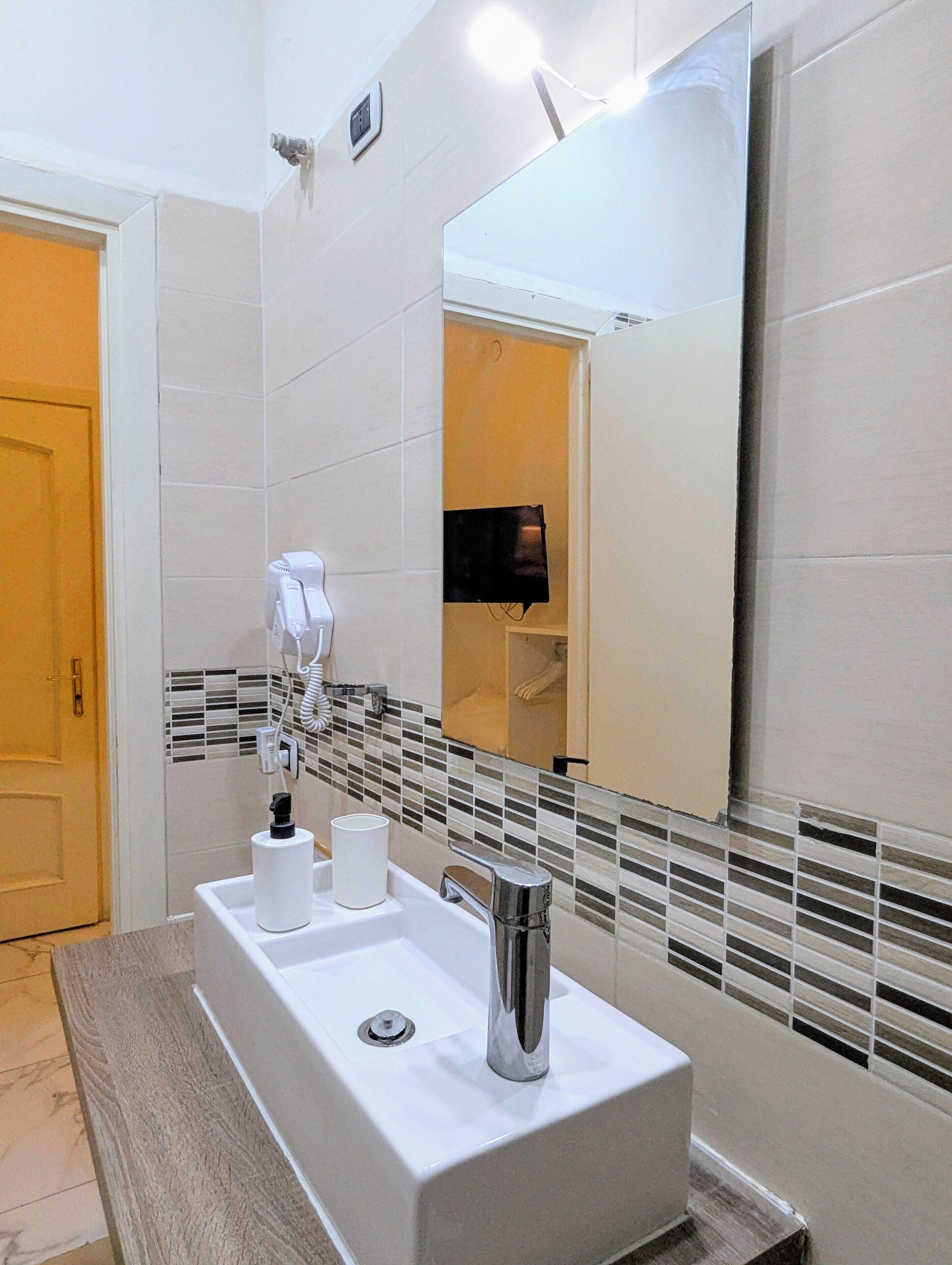 A modern bathroom with a rectangular sink, a mirror, and a towel dispenser.