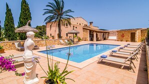 A pool area with lounge chairs, a statue, and a stone building with a thatched roof. - Gorgeous home in Felanitx with private swimming pool, can be inside or outside (Felanitx)