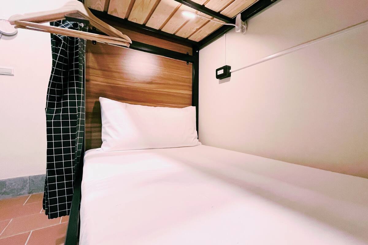 A single bed with a wooden headboard, a white pillow, and a black and white checkered curtain.