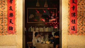 A restaurant interior with a table set for three people, a bookshelf filled with books, and red banners with Chinese characters. - KIVALA Hostel (Jincheng)