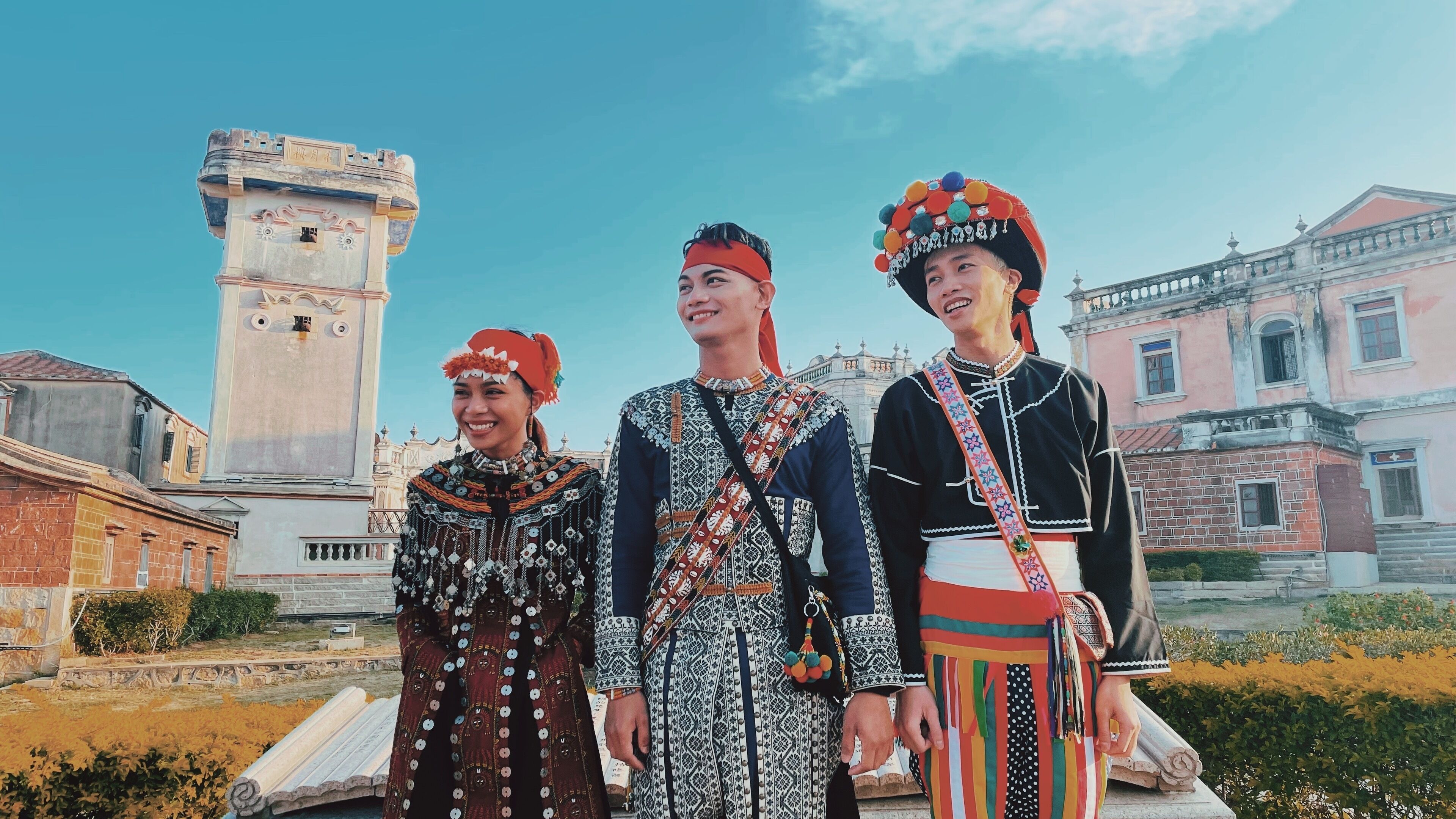 Un groupe de personnes, vêtues de costumes traditionnels, se tient devant un bâtiment historique surmonté d’une tour.