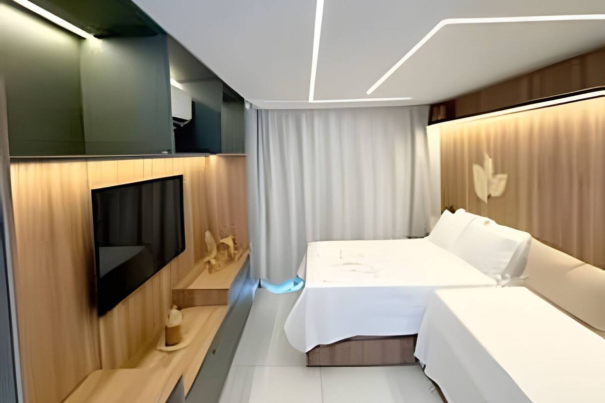 A modern hotel room with a bed, a flat-screen TV, and a wooden accent wall.