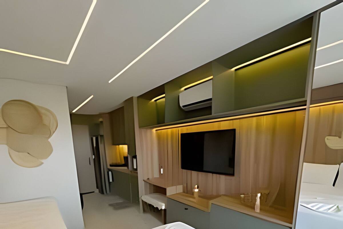 A modern hotel room with a large bed, a flat-screen TV mounted on a wooden panel, and a small seating area with a table and chairs.