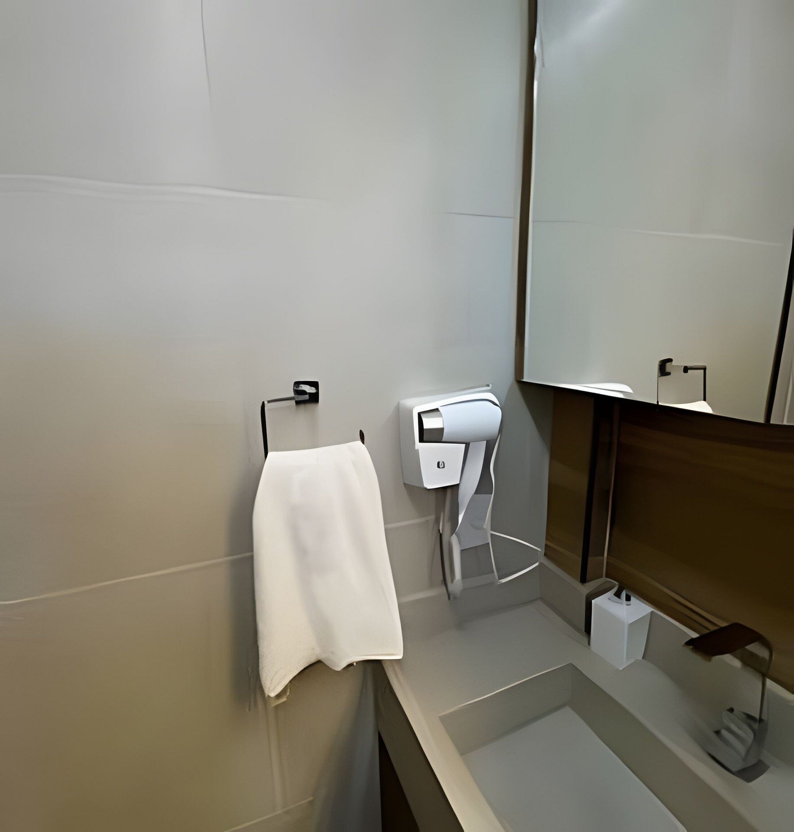 A modern bathroom with a white towel hanging on a hook, a towel dispenser, and a mirror above the sink.
