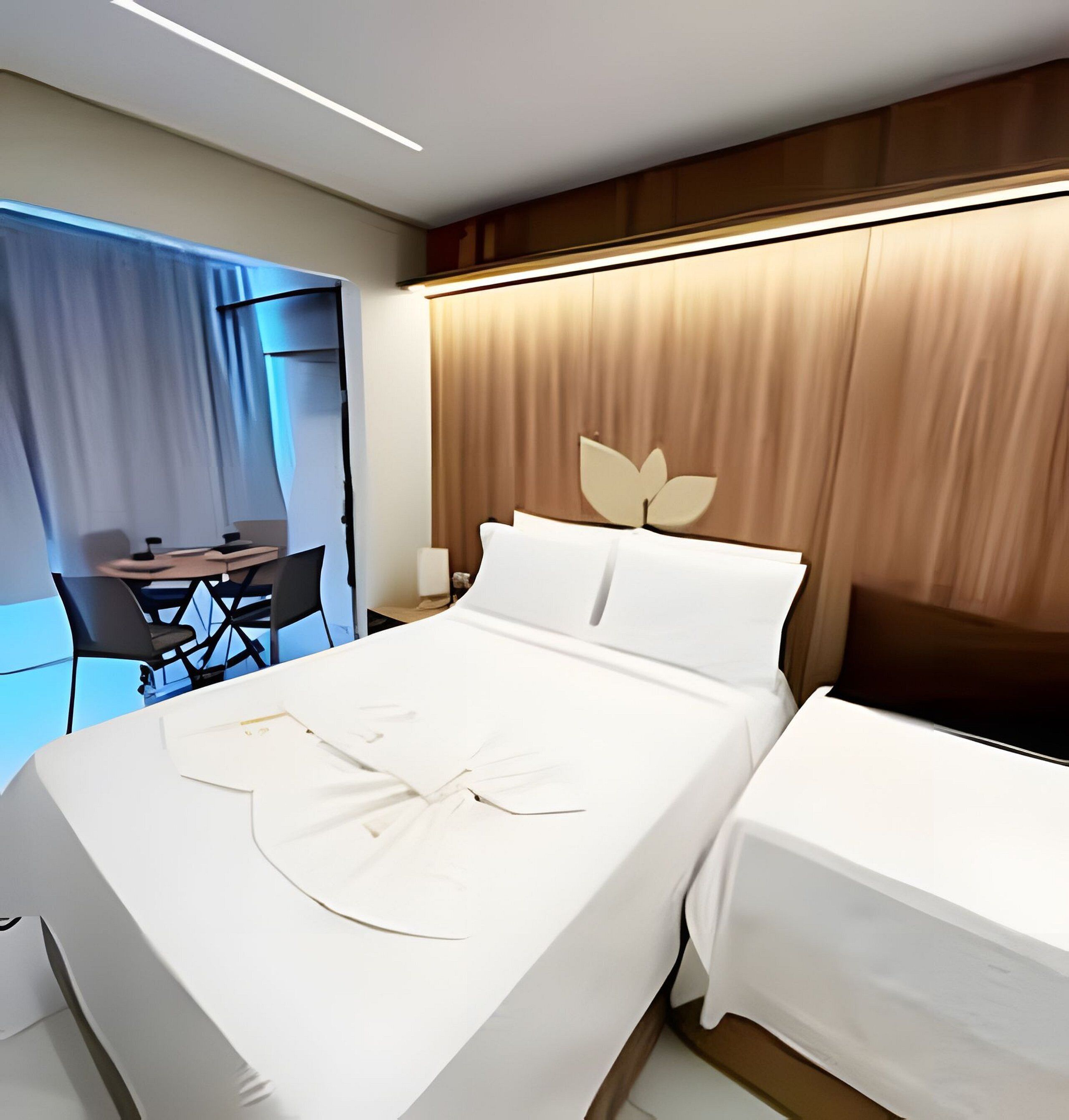 A hotel room with a neatly made bed, a desk with a chair, and a large window with curtains.