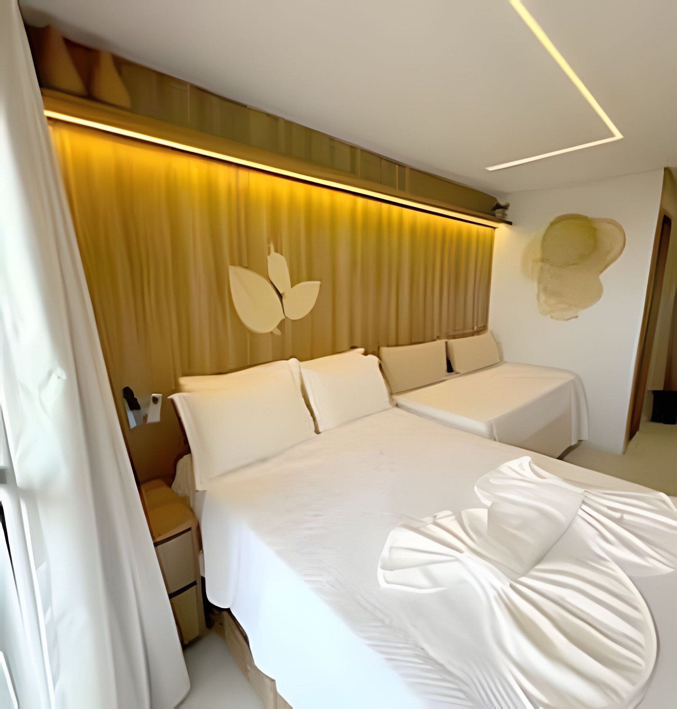 A modern hotel room with a large bed, a bedside table, a nightstand, and a wall-mounted light fixture.
