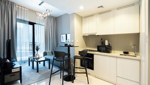 A modern kitchen with white cabinets, a black countertop, and a built-in stove. There is a dining area with a table and chairs, and a large window with curtains. - KeyRock Living - Elegant Lake View Apt (Dubai)