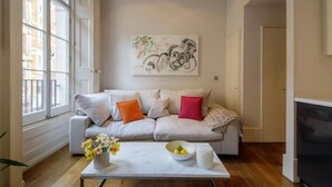 Een woonkamer met een bank, een bijzettafeltje met bloemen en een schilderij aan de muur.