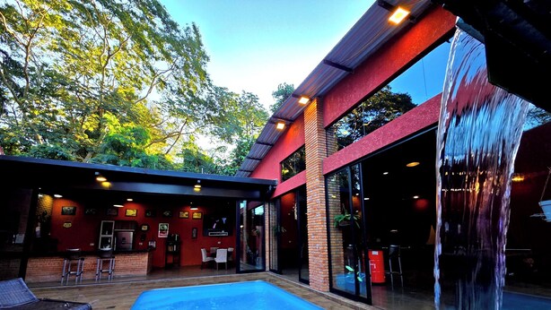 Una piscina exterior con cascada, rodeada por un porche techado con asientos y una zona de bar.