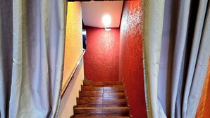 Una escalera de madera con cortinas atadas en la parte superior, que conduce a una habitación con paredes rojas y una lámpara en el techo.