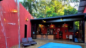 Un área de piscina con sillones de descanso, un bar y una cocina visibles a través de las paredes de vidrio.