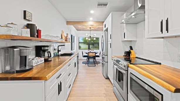 Una cucina moderna con mobili bianchi, elettrodomestici in acciaio inossidabile e un piano di lavoro in legno.