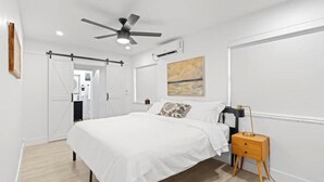 Una camera da letto con un letto, un comodino, una ventola a soffitto e un'opera d'arte appesa al muro.