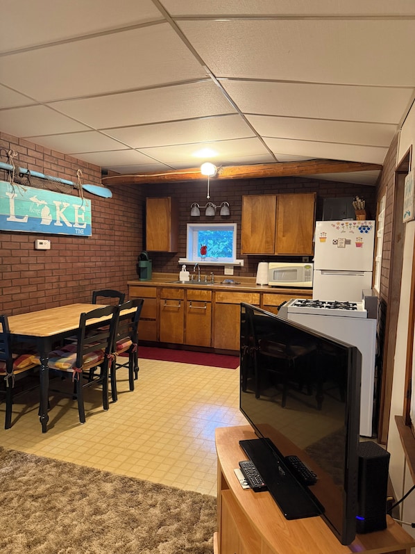 Una cocina compacta con gabinetes de madera, microondas integrado y un refrigerador con imanes.