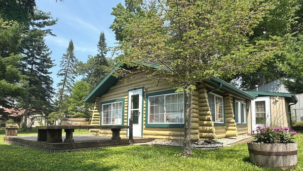 Una cabaña de troncos con un porche, una mesa de picnic y un parterre de flores.
