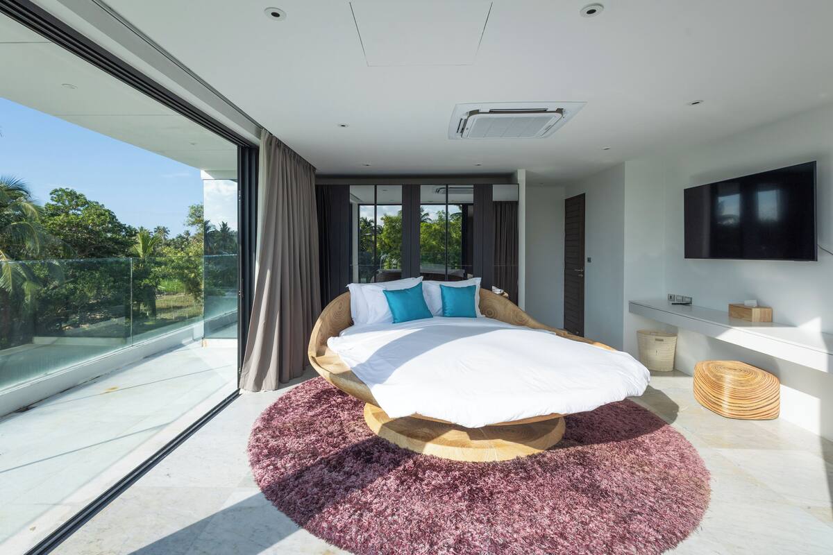 Camera da letto moderna con un letto grande, una porta vetrata che conduce a un balcone e una TV a parete.
