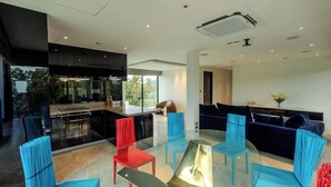 A modern interior with a glass dining table surrounded by chairs, a kitchen area with a large island, and a dark-colored sofa.