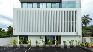 A modern building with a flat roof, large windows, and a series of planters with green plants in front.