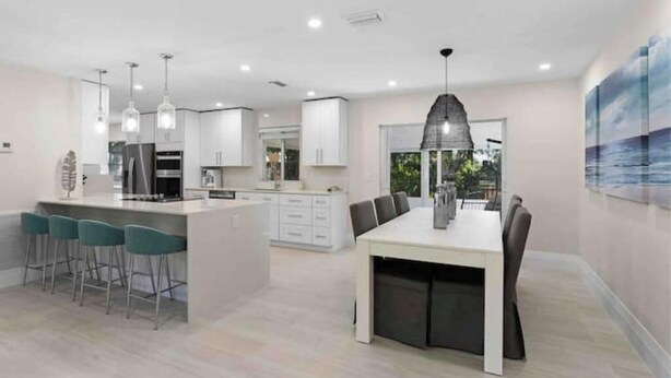 A modern kitchen with white cabinets, a central island with bar stools, and pendant lighting. - Walking distance to the beach & close to downtown! (Boca Raton)