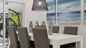 A dining area with a white table, grey upholstered chairs, and a hanging pendant light. - Walking distance to the beach & close to downtown! (Boca Raton)