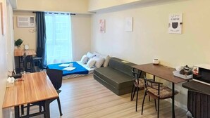 A modern living room with a sofa, a dining table, and a small kitchen area. - Avida Riala at Cebu IT Park Spacious 1 Bedroom With Fast Wifi Smart TV For 6 (Cebu City)