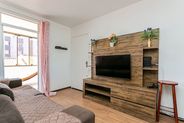 A modern living room with a large flat-screen TV, wooden entertainment unit, and a balcony with a hammock. - Beautiful apt 750 m From the Beach of Ingleses Lgr204 (Florianópolis)