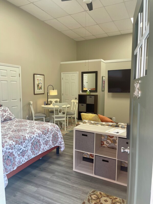 A bedroom with a bed, a desk, a chair, a TV, and a storage unit.
