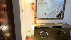 A hallway with a wooden door, a mirror with a decorative frame, a vanity with a round mirror, and a patterned floor. - Luxurious West London Retreat With Hot Tubs & Easy Access to Central London (Greenford)