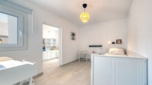 Een lichte, moderne kamer met een wit bureau, een stoel, een radiator en een hanglamp.