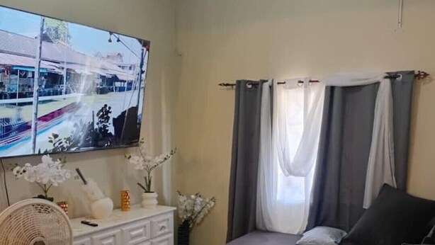 Een woonkamer met een bank, een aan de muur bevestigde televisie, een ventilator en een decoratief vloerkleed.