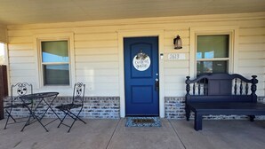 A house with a blue door, a number '2613' above it, a bench, and a small table with chairs on the porch.