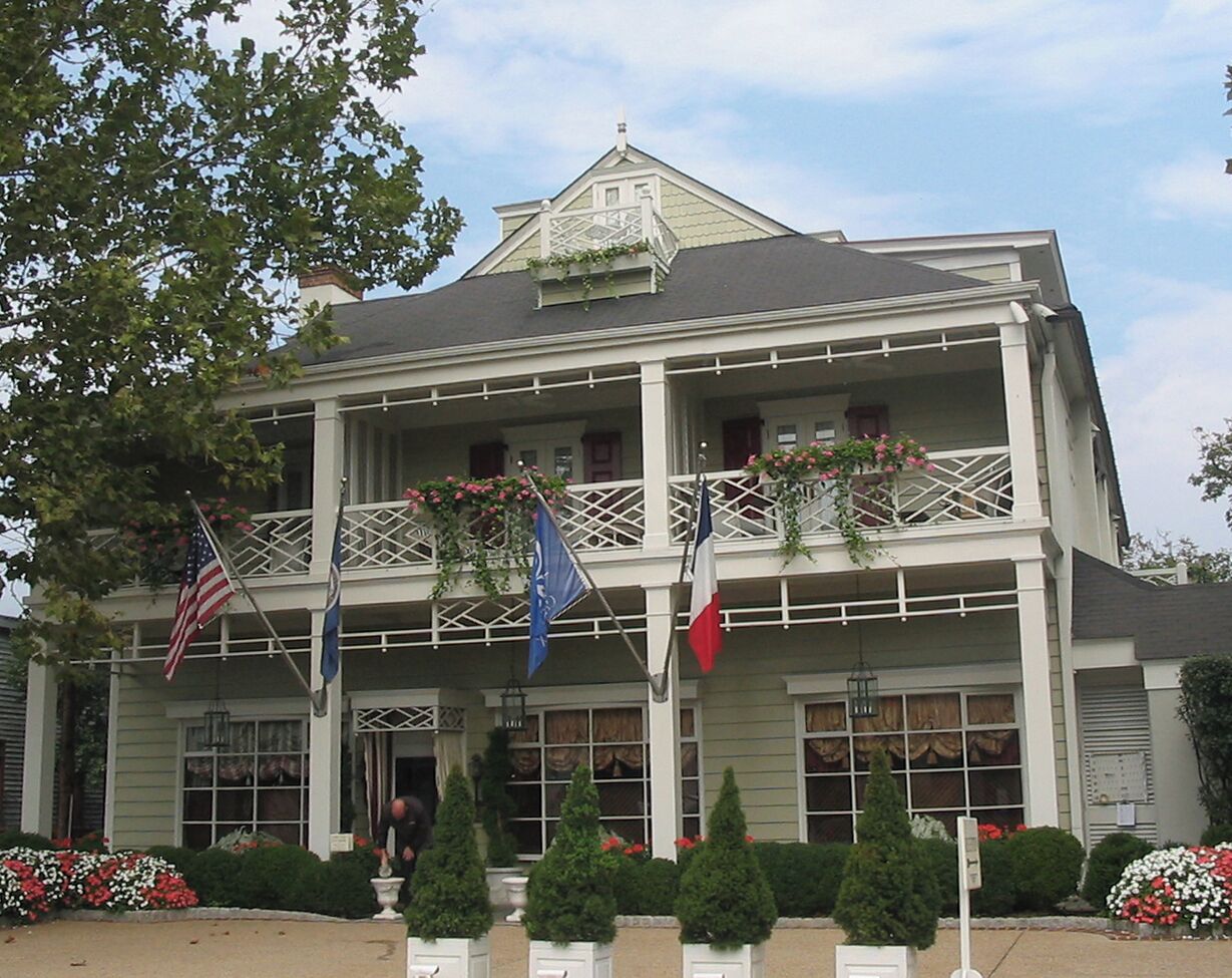 A two-story building with a balcony, flags, and a well-maintained garden.