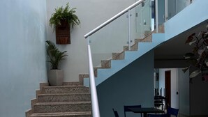 A staircase with granite steps, a metal handrail, and a glass railing leading to an upper floor. There is a dining area with a table and chairs below the stairs. - Casa COP30 14 leitos, Condominio Segurança armada 24h (Tapanã Belém)