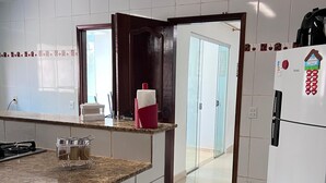 A kitchen with white tiled walls, a granite countertop, a gas stove, a refrigerator, and a gas cylinder. - Casa COP30 14 leitos, Condominio Segurança armada 24h (Tapanã Belém)