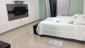 A modern hotel room with a large bed, a flat-screen TV mounted on the wall, a small desk, and a window with curtains. - Casa COP30 14 leitos, Condominio Segurança armada 24h (Tapanã Belém)