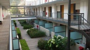 Un hôtel à plusieurs étages doté d’une cour intérieure avec une terrasse en bois, entourée de verdure et de plantes en pot.