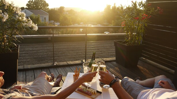 Une terrasse avec une table dressée pour deux personnes, agrémentée d’une bouteille de champagne, de verres et d’une assiette de nourriture.