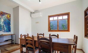 A dining area with a wooden table and chairs, a painting on the wall, and a window with a view of greenery. - House With Pool Near the Beach Jde792 (Florianópolis)