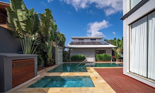 Una casa moderna con piscina, paneles solares y exuberante vegetación tropical.